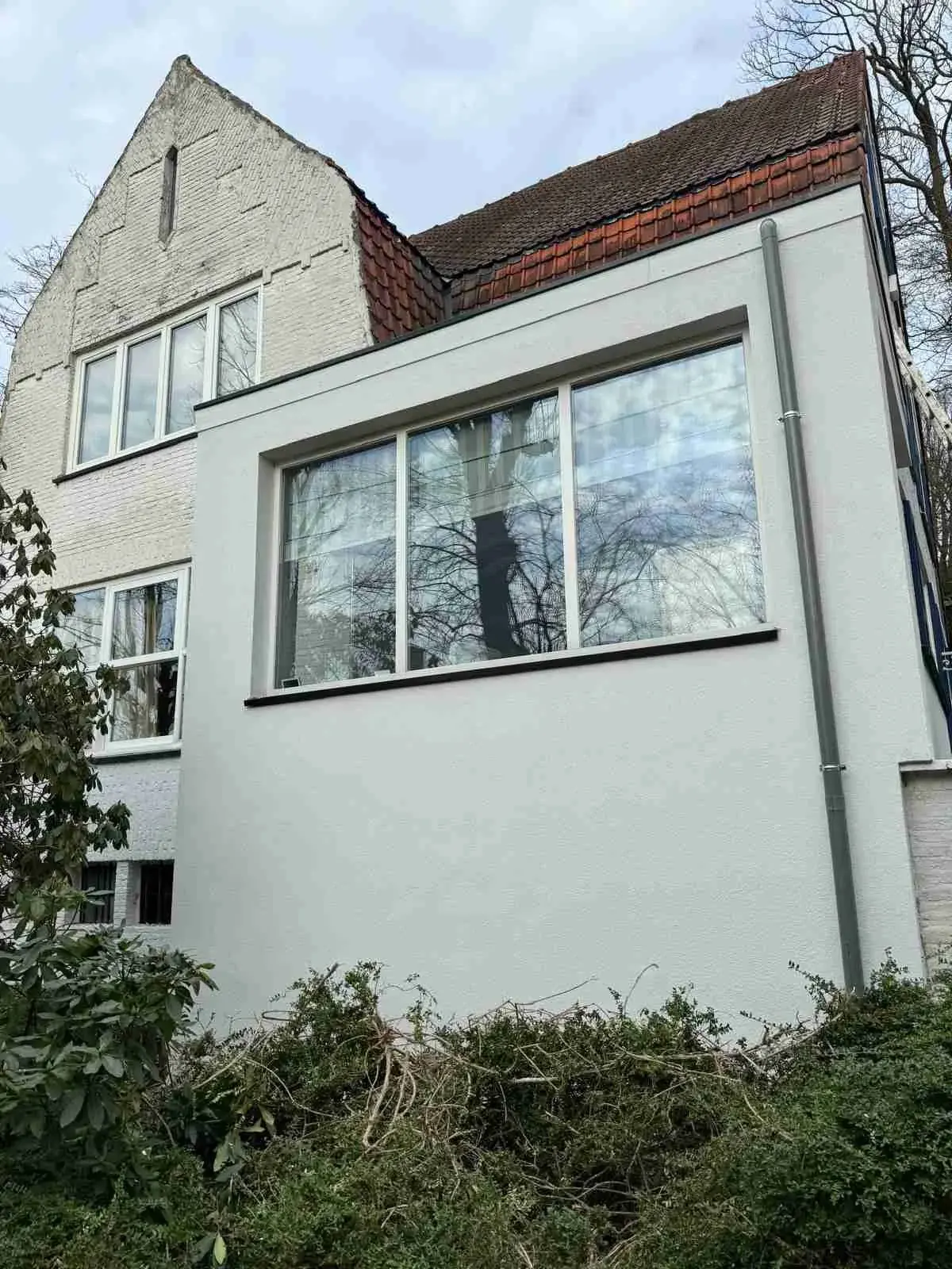 Façade blanche rénovée d’une maison avec grande baie vitrée