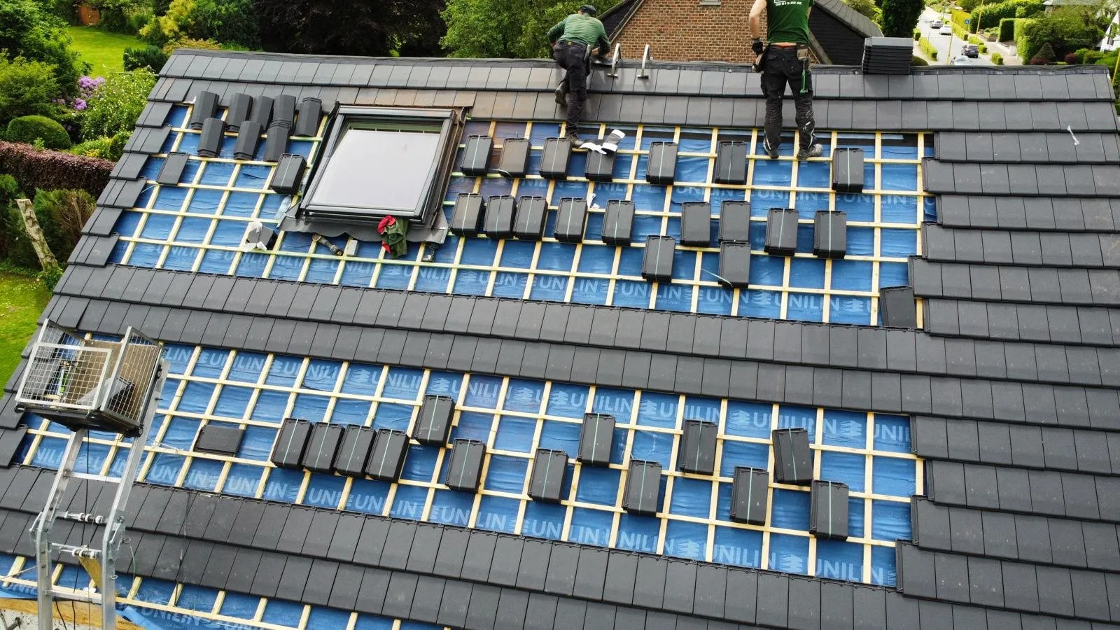 Vue aérienne d'une toiture en rénovation : panneaux isolants et lattage bois, tuiles plates en attente de pose